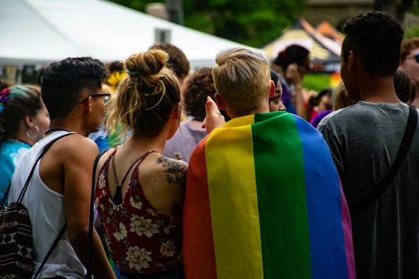 A group of people at a pride celebration. One wears a rainbow flag