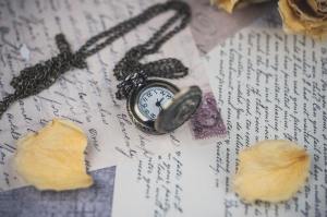 A brass pocket watch on a chain rests over handwritten letters and flower petals. 