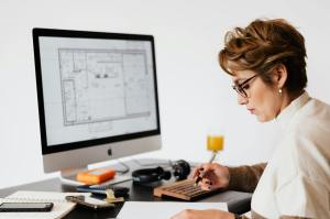 A white woman with brown hair at a computer revising drawings of a floorplan. 
